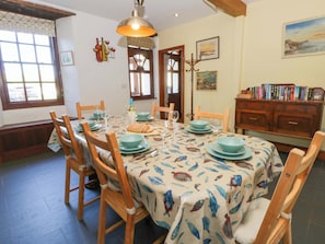 A dining area with a table set for four, wooden chairs, a patterned tablecloth, and a bookshelf with books.