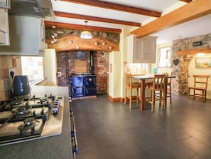 A kitchen with a gas stove, wooden chairs, a stone wall, and a brick fireplace.