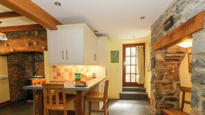 A kitchen with a stone wall, wooden chairs, a table, and a door with a window. - Parrog Stores (Newport)