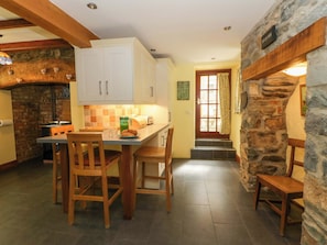 A kitchen with a stone wall, wooden chairs, a table, and a door with a window.
