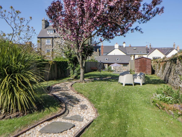 A residential garden with a pathway, a tree, and a house in the background.