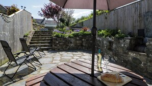 A patio with a stone floor, wooden furniture, and a table with a loaf of bread and wine glasses. - Parrog Stores (Newport)