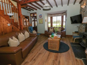 A cozy living room with a brown leather sofa, a blue armchair, a wooden coffee table with a tray, and a fireplace.