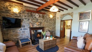 A cozy living room with stone walls, a fireplace, leather sofas, and a television. - Parrog Stores (Newport)