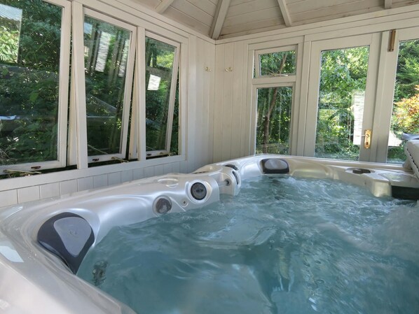 A hot tub with multiple jets, large windows, and a view of greenery outside.