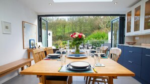 A dining area with a wooden table set for four, a vase of flowers, and a view of greenery outside. - 5 Seabird Close, Little Haven (Little Haven)