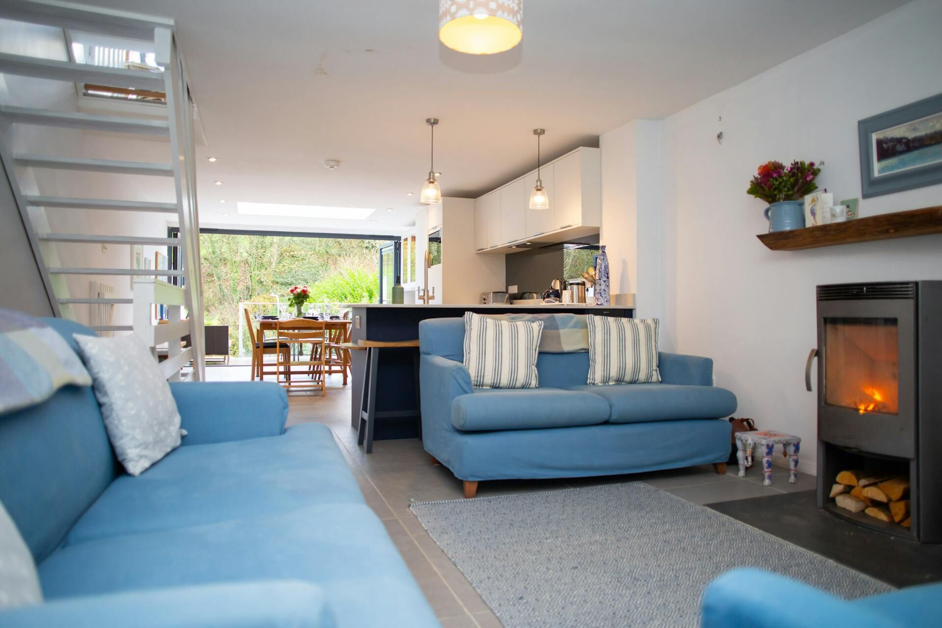 A modern living room with a blue sofa, a fireplace, and a kitchen area visible through an open door.