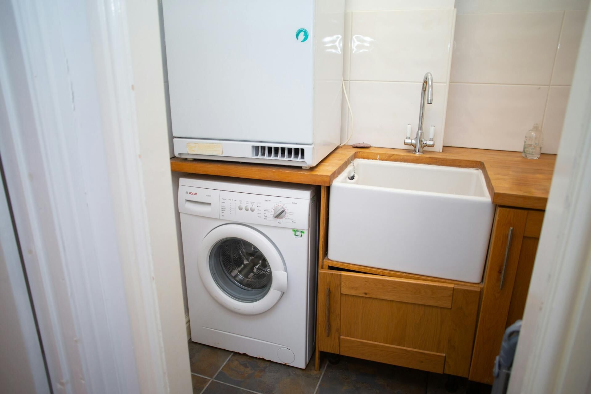 A compact laundry room with a Bosch washing machine, a small sink, and wooden cabinets.