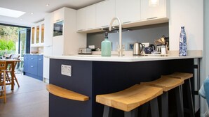 A modern kitchen with a central island, bar stools, and a dining area with a table and chairs. - 5 Seabird Close, Little Haven (Little Haven)