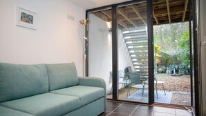 A modern living room with a teal sofa, a floor lamp, and a sliding glass door leading to an outdoor patio area with chairs and a table. - 5 Seabird Close, Little Haven (Little Haven)