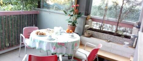 A small balcony with a round table and chairs, a potted plant, and a view of trees.