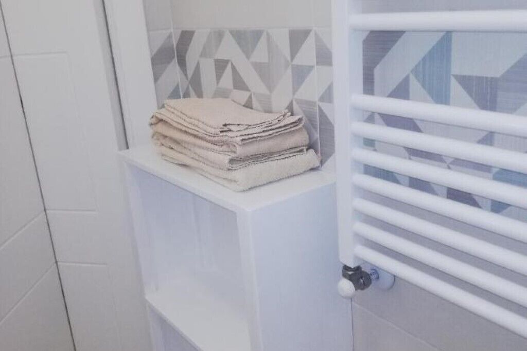 A bathroom with a towel rack holding folded towels, a white cabinet, and a geometric-patterned tile backsplash.
