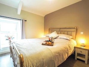 A neatly made bed with pillows, a bedside table with a lamp, and a tray with breakfast items. - Bryndalis, Aberaeron (Dihewyd)