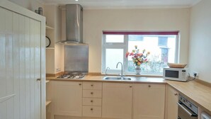 Une cuisine moderne équipée d’une cuisinière à gaz, d’une hotte en acier inoxydable, d’un évier à deux bacs et d’un four à micro-ondes.