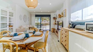 Una cocina moderna con armarios blancos, un comedor con sillas de madera y un amplio ventanal con vista a palmeras.