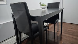 A modern dining area with a dark wooden table and chairs, a white bowl with a plant, and a white wall. - Grandiosely Pleasant Suite 2 (Hempstead)