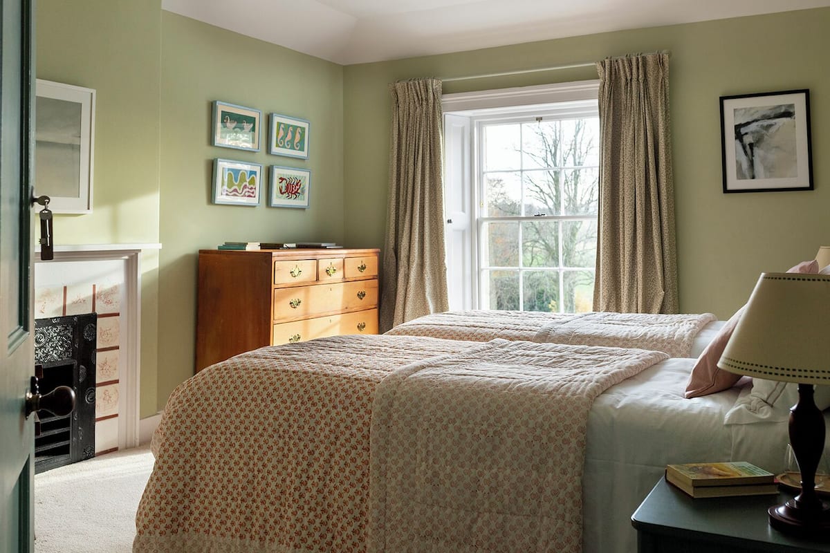 Une chambre avec deux lits, une commode, une lampe et une cheminée.