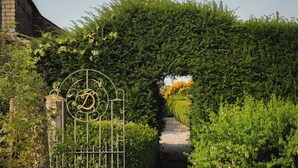 Un sendero en el jardín que atraviesa un arco de seto con una puerta de metal que lleva un monograma.