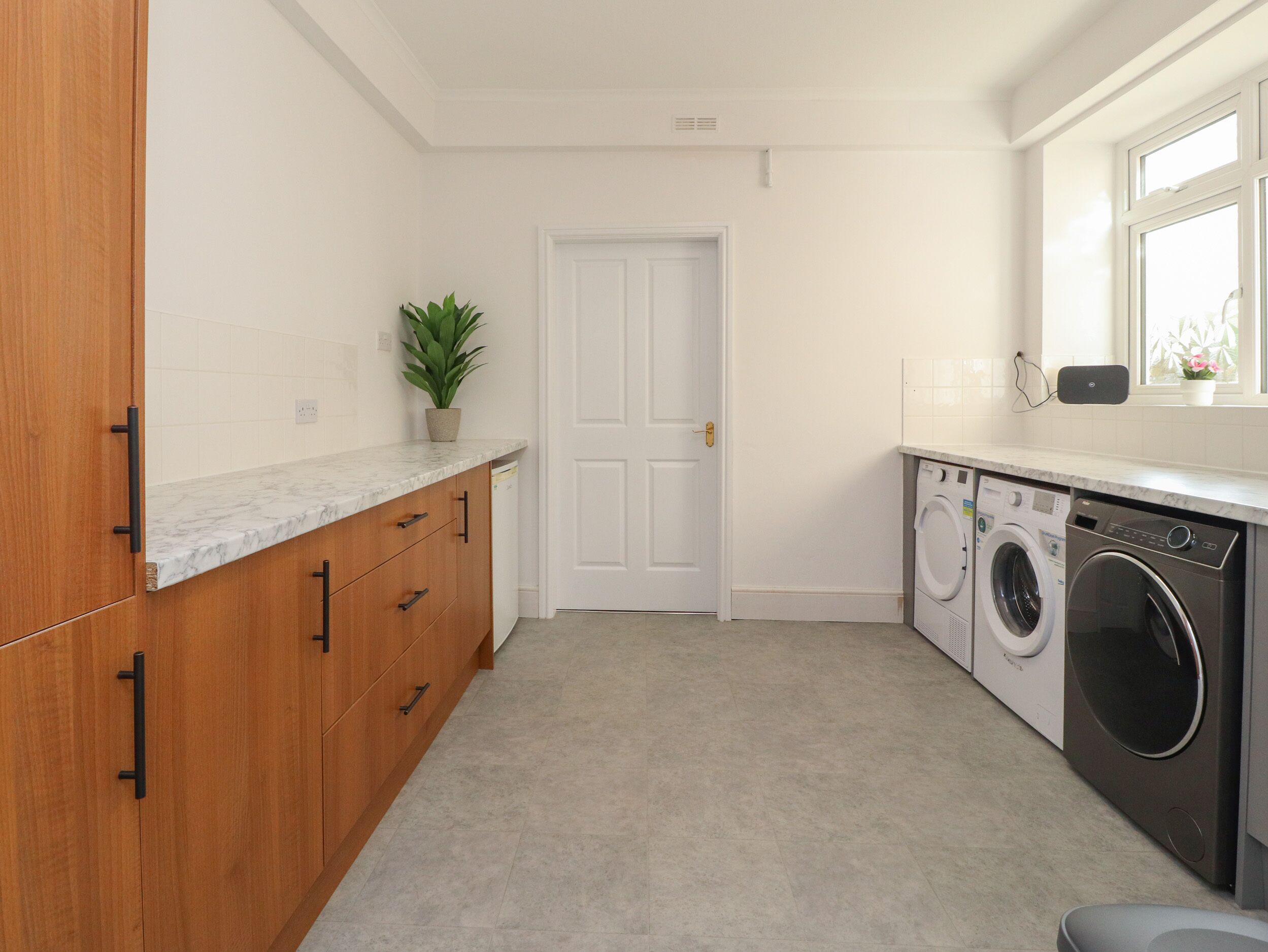 A compact kitchen with wooden cabinets, a marble countertop, a potted plant, a white door, and a built-in washer and dryer.