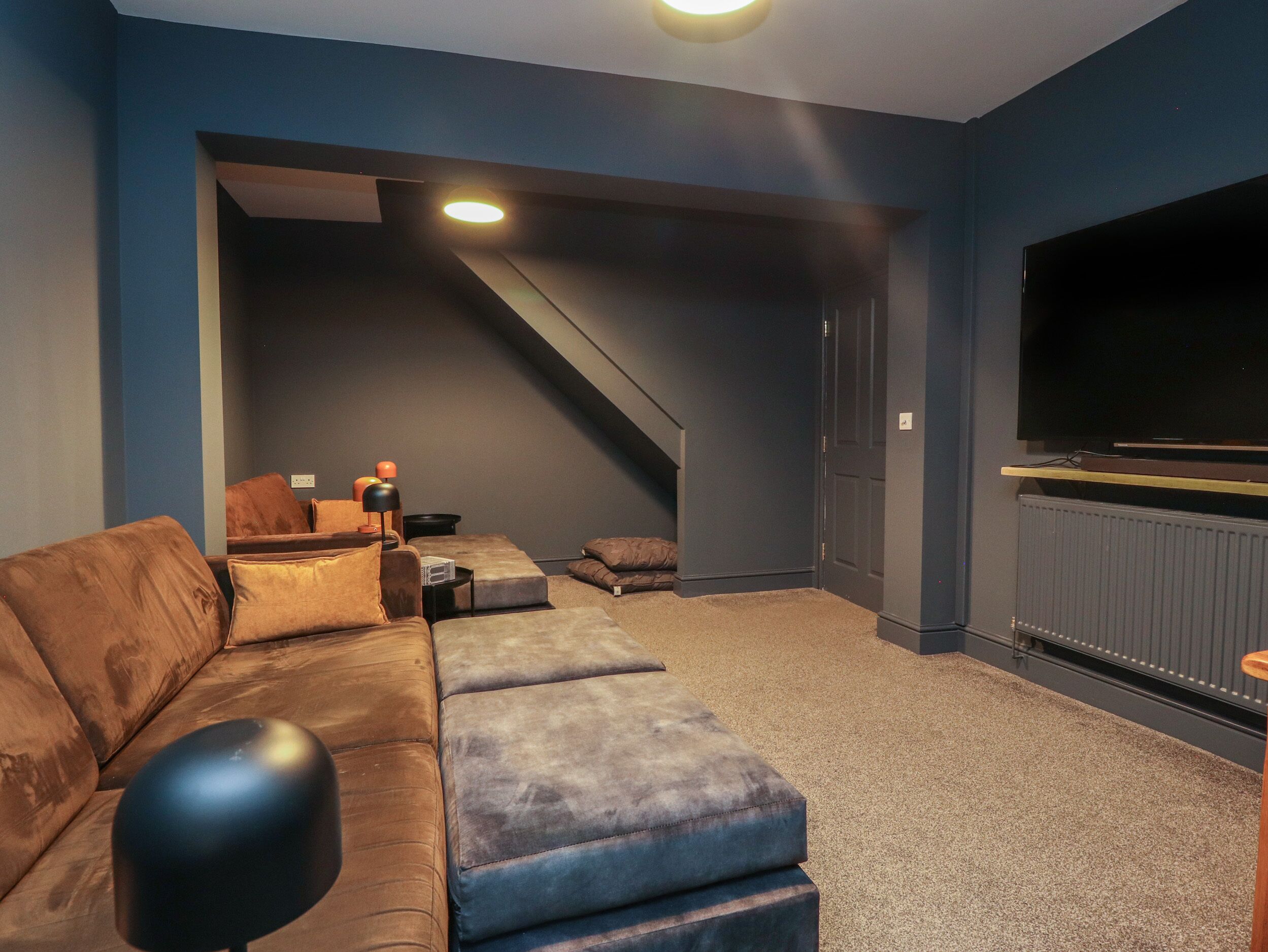 Un salon moderne avec un canapé d’angle, un pouf et un téléviseur à écran plat.