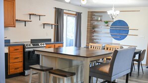 Ett modernt kök med en central köksö, trästolar till bardisken, ett matbord med stolar och en unik väggdekoration.