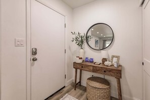A hallway with a white door, a round mirror, a wooden console table, and a wicker basket.
