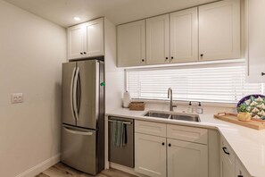 Una cocina moderna con un refrigerador de acero inoxidable, un lavamanos con ventana arriba y muebles de color claro.