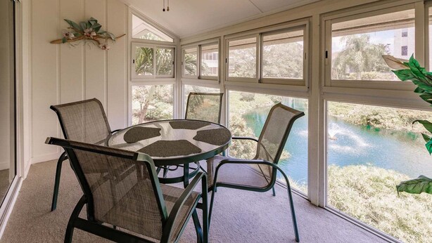 Ein Zimmer mit rundem Tisch und vier Stühlen, großen Fenstern mit Blick auf ein Gewässer und einem Deckenventilator.
