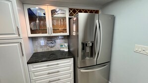 A kitchen with a stainless steel refrigerator, white cabinetry, a clock, and a water dispenser.