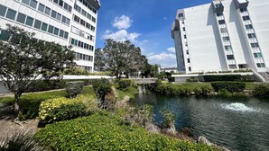 A modern building complex with a river and greenery in the foreground.