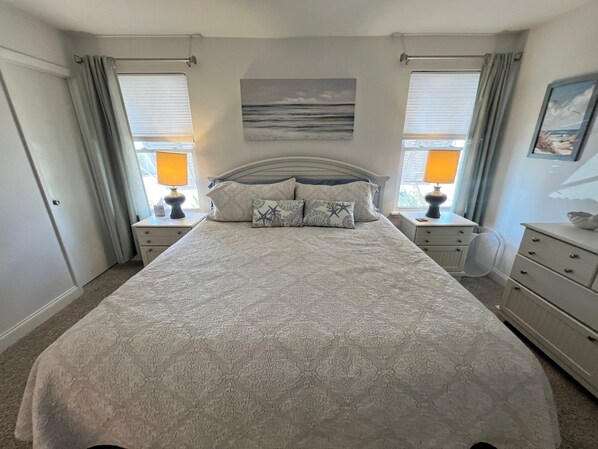 A bedroom with a large bed, two bedside tables with lamps, a headboard, and a window with curtains.