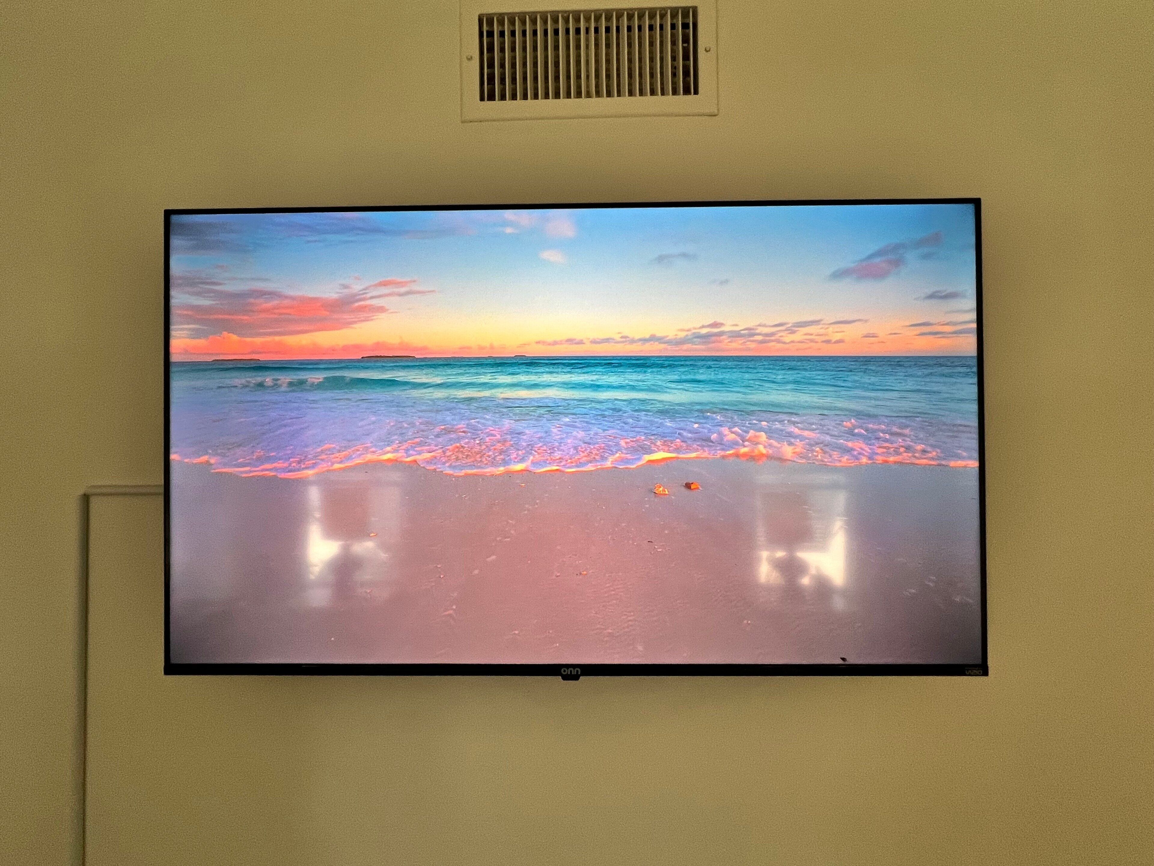 Un televisor montado en la pared mostrando una escena de playa con olas y un atardecer.