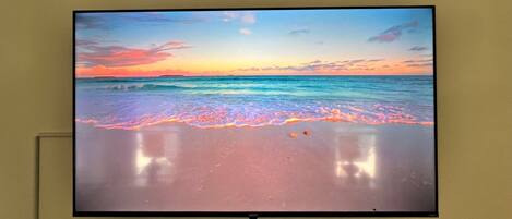 Un televisor montado en la pared mostrando una escena de playa con olas y un atardecer.