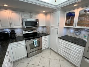 A modern kitchen with stainless steel appliances, white cabinetry, and a tiled backsplash.