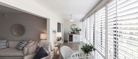 A modern living room with a sofa, armchairs, a glass coffee table, and a dining area with a small table and chairs.
