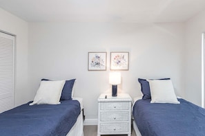 A bedroom with two beds, a nightstand with a lamp, and two framed floral artworks on the wall.