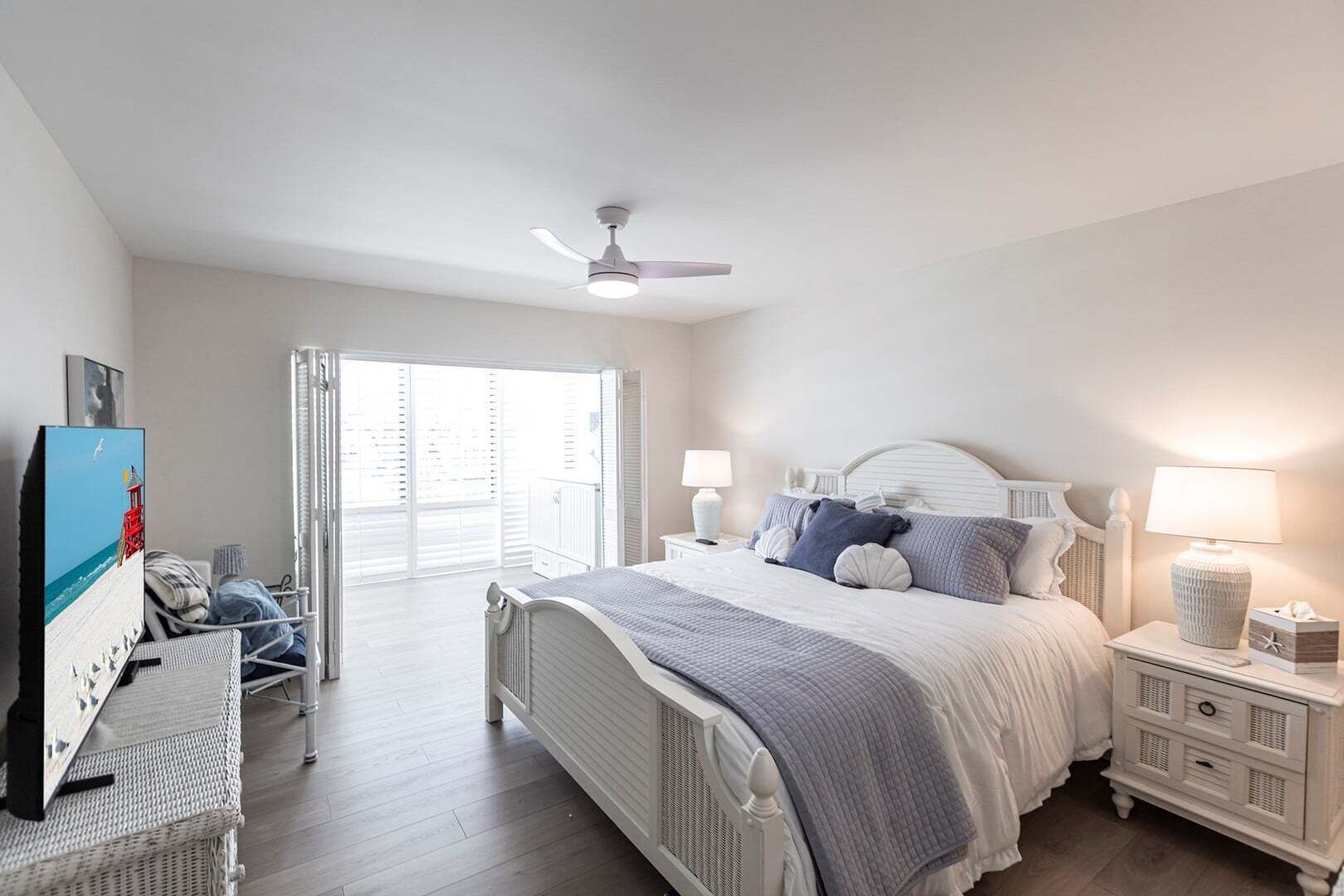 A bedroom with a bed, bedside tables, a ceiling fan, and a view through a window.