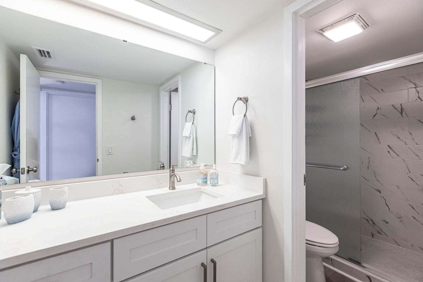 Une salle de bain moderne avec un grand miroir, un meuble-lavabo blanc et un espace douche.
