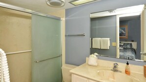 Un baño con mampara de vidrio, lavabo con espejo y toallero.