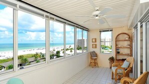 Un balcón con vista a la playa, mobiliario de mimbre y un ventilador de techo.