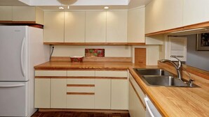 Cocina compacta con armarios blancos, encimera de madera, lavamanos empotrado y ventilador de techo.