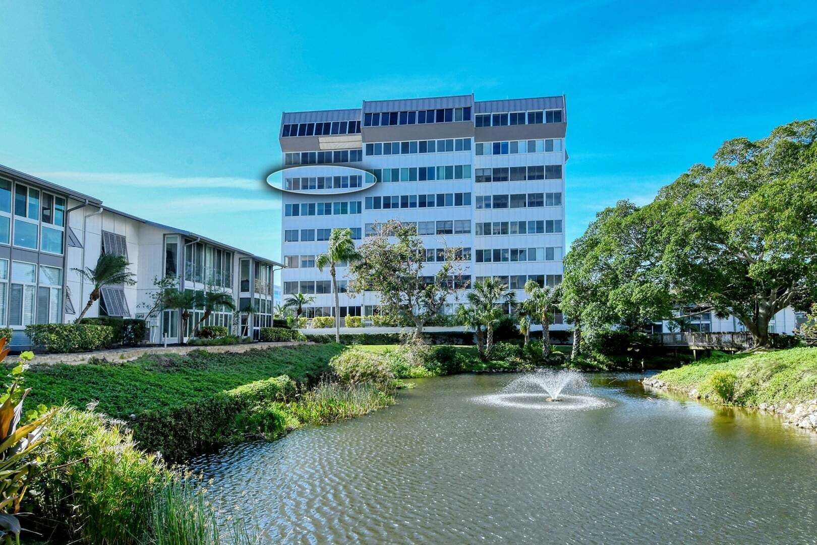 En modern byggnad med en central innergård med en fontän, omgiven av grönska och palmer.