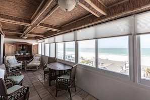 Ein Zimmer mit Blick auf den Strand, mit Korbmöbeln, einem Tisch und einer Decke mit Bambusbalken.