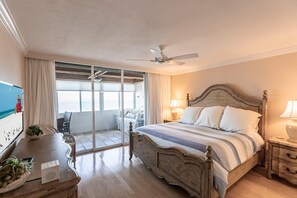 Ein Schlafzimmer mit Bett, Nachttischen, Deckenventilator und Blick auf den Strand.