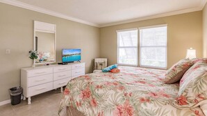 A bedroom with a bed, dresser, TV, and windows.