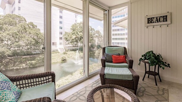 A room with a large window overlooking a body of water and buildings, wicker furniture, and a sign that reads 'BEACH'.