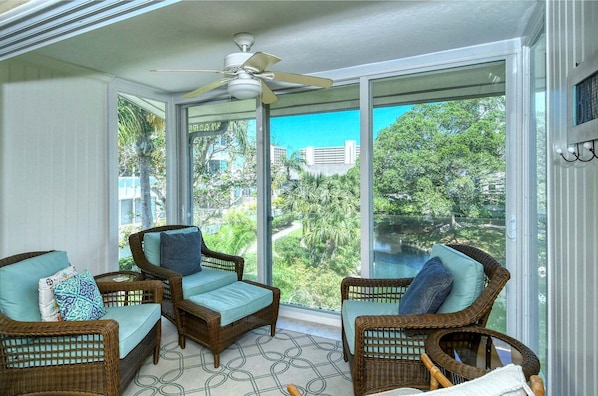 A sunlit room with wicker furniture, large windows, and a ceiling fan.