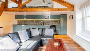 A modern loft apartment with a loft bed, a kitchen with a stone backsplash, a gray sofa with cushions, and a wooden coffee table. - Sedbergh Penthouse - Kingbed - Tv - Wifi (Sedbergh)