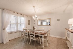 A dining room with a wooden table and chairs, a chandelier, a mirror, and a window with curtains. - 1081 PD - Standard Plus - Unwind in Our Spacious Townhome Oasis (Siesta Key)