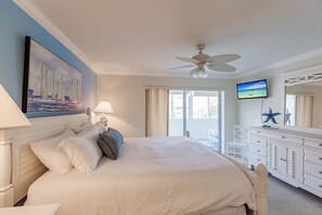 Ein Hotelzimmer mit Bett, Deckenventilator, Fernseher, einem Gemälde und einem Balkon mit Blick.